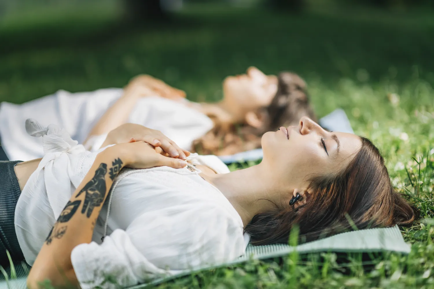 Deux femmes allongées dans l'herbe qui pratiquent des exercices de sophrologie pour apaiser l'anxiété